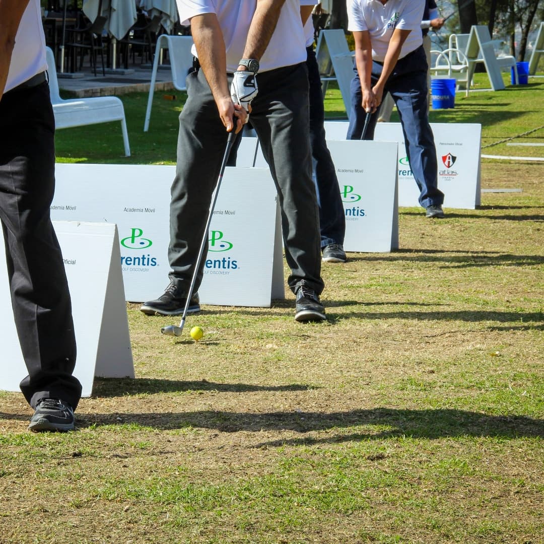 Prentis Golf students holding their clubs at outdoor hitting stations lined with Prentis signs
