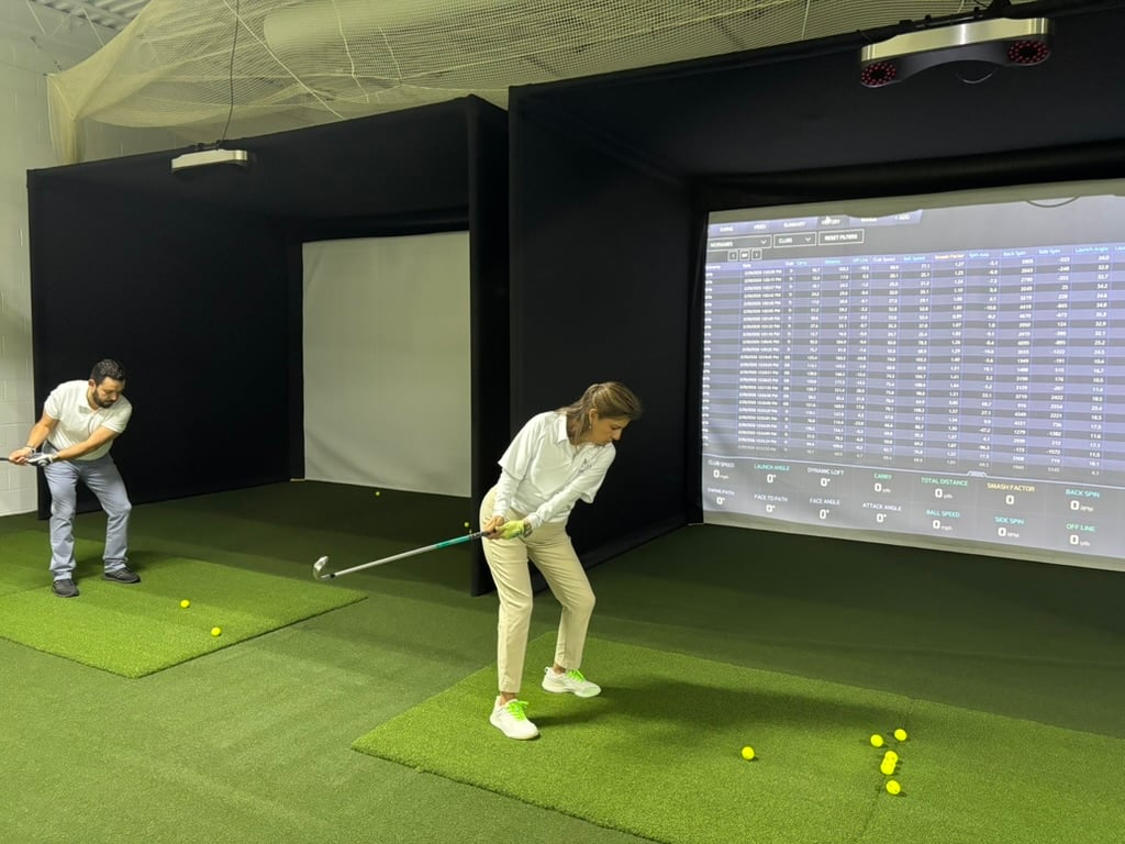 Two Prentis Golf students swinging on indoor hitting mats in front of a launch monitor screen full of shot data
