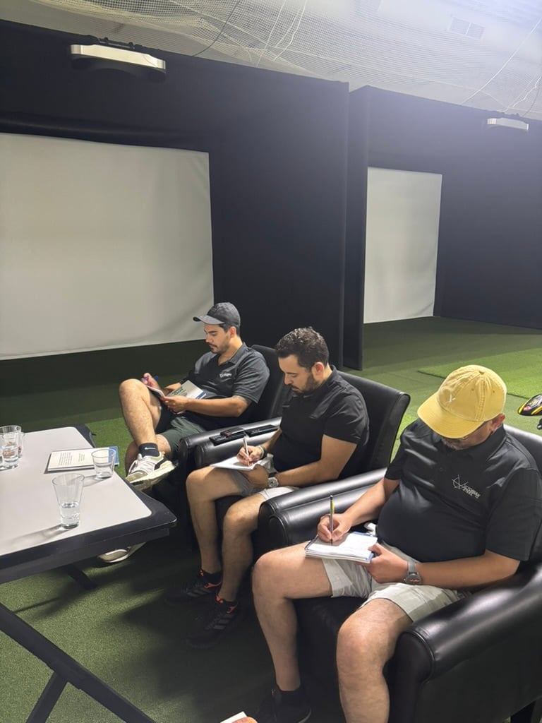 Three Prentis Golf students in black polos taking notes in leather armchairs in front of the simulator screens